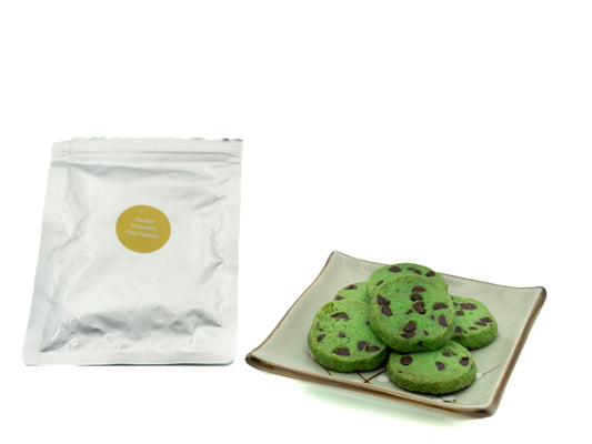Green cookies with chocolate chips on a plate next to a clear packaging bag on a white background