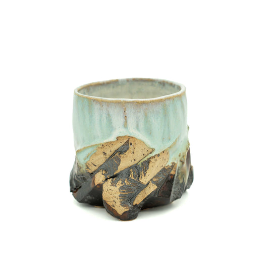 A handmade ceramic cup with a light blue-green glaze on the upper half and a rustic, rough-textured dark brown and tan lower half, shown on a plain white background.