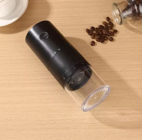 Black and clear portable coffee grinder on a wooden surface with coffee beans nearby